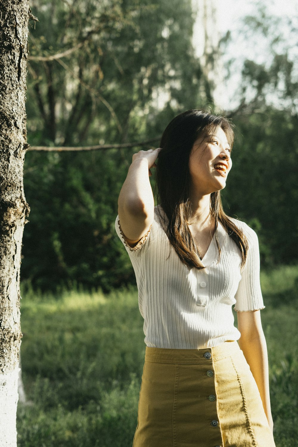 Mujer con camisa blanca y pantalones cortos amarillos de pie junto a un árbol durante el día