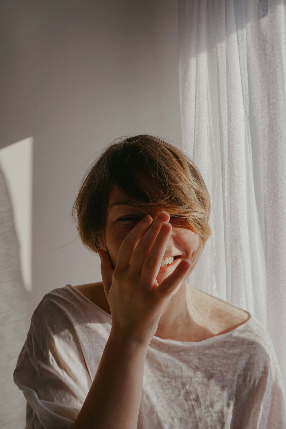 woman in gray crew neck shirt covering her face with her hand