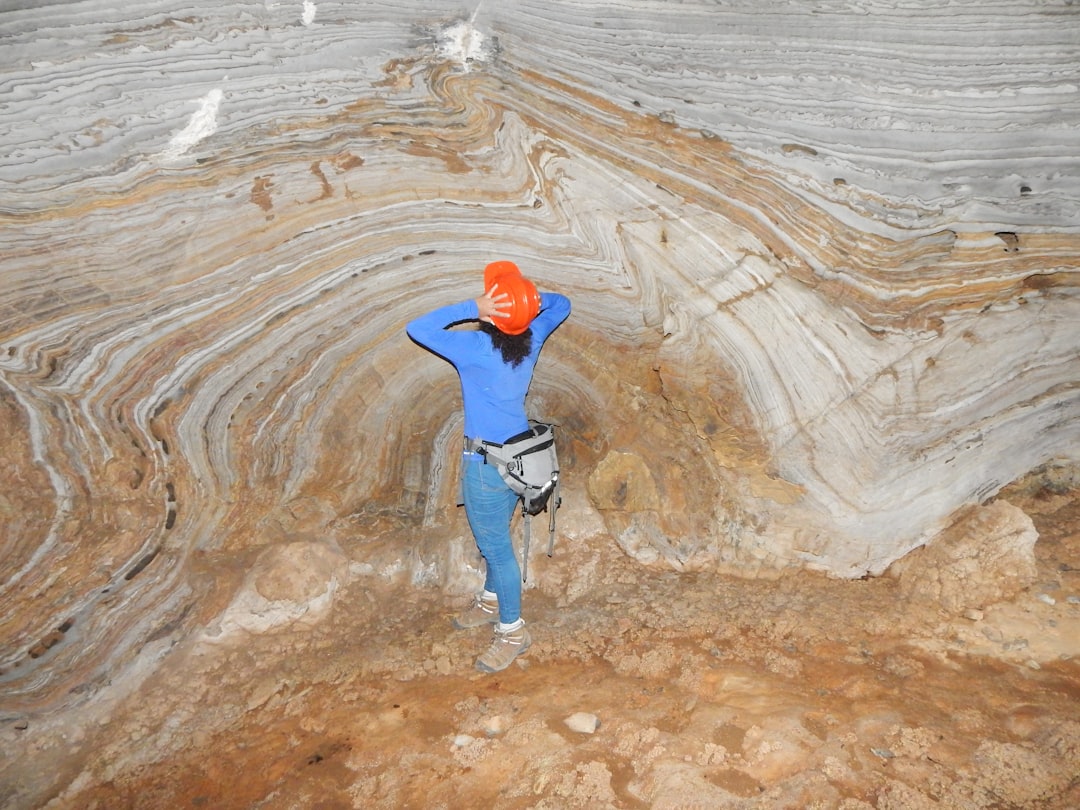 man in blue jacket and blue denim jeans standing on brown rock formation during daytime, cave speleology geology