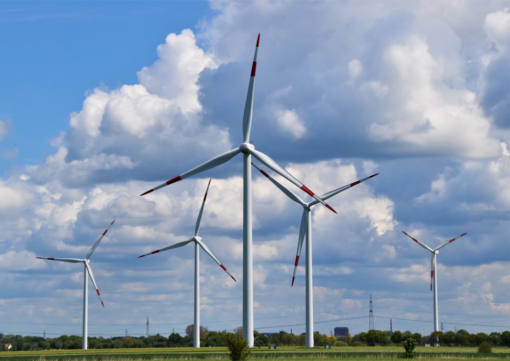 turbinas eólicas brancas no campo de grama verde sob o céu nublado azul e branco durante o dia