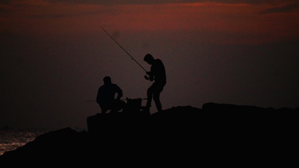 silhouette of 3 person on rock during sunset