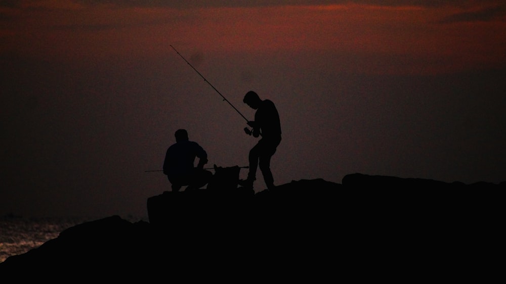 Silueta de 3 personas en la roca durante la puesta del sol