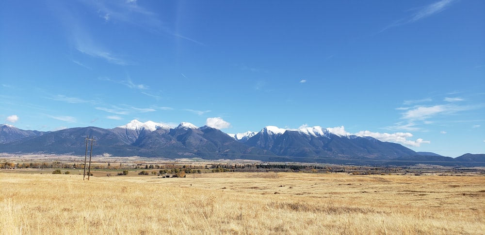 brown grass field near snow covered mountains under blue sky during daytime