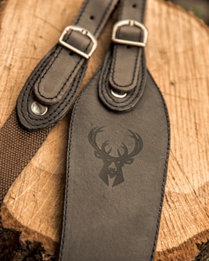 A close-up view of two leather straps with buckles placed on a wooden surface. One of the straps features an embossed design of a deer's head with antlers.