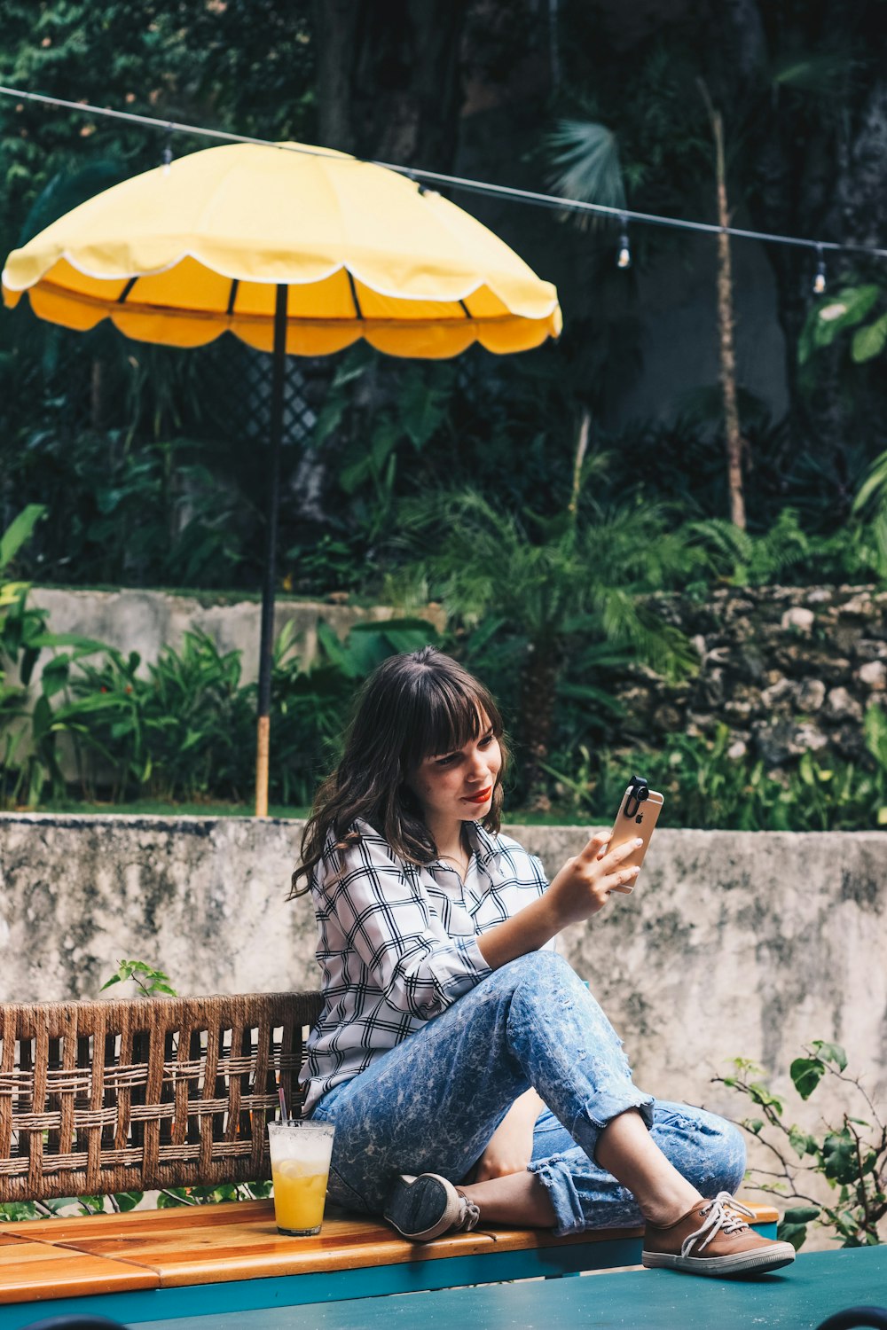 woman in blue denim jeans sitting on brown wooden bench holding smartphone