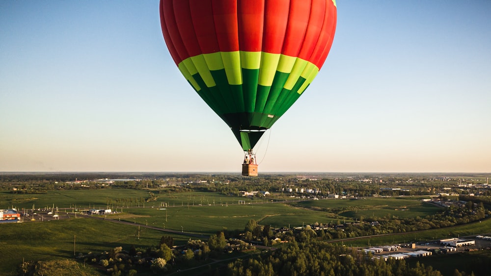 mongolfiera rossa, verde e blu che sorvola il campo di erba verde durante il giorno