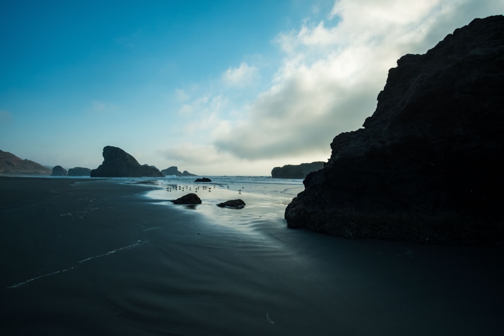 black rock formation on sea water under blue sky and white clouds during daytime