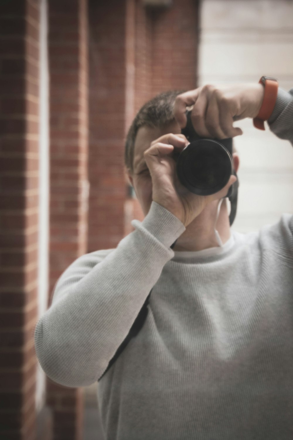 woman in gray sweater holding black camera lens