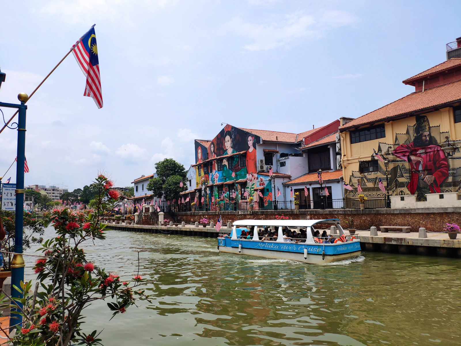 Barco turístico en el río de Melaka frente a fachadas históricas cubiertas de murales
