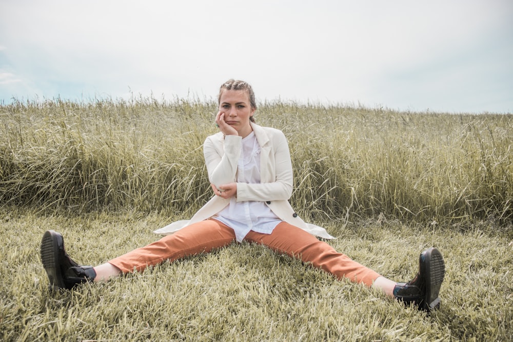 woman in white long sleeve shirt and orange pants sitting on green grass field during daytime