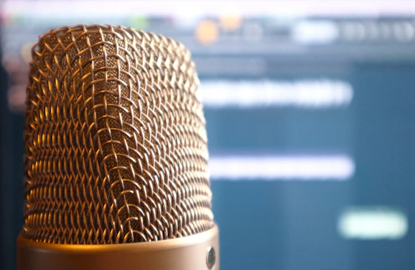 A close-up photo of a sleek microphone surrounded by vintage mic stands in a cozy recording studio.