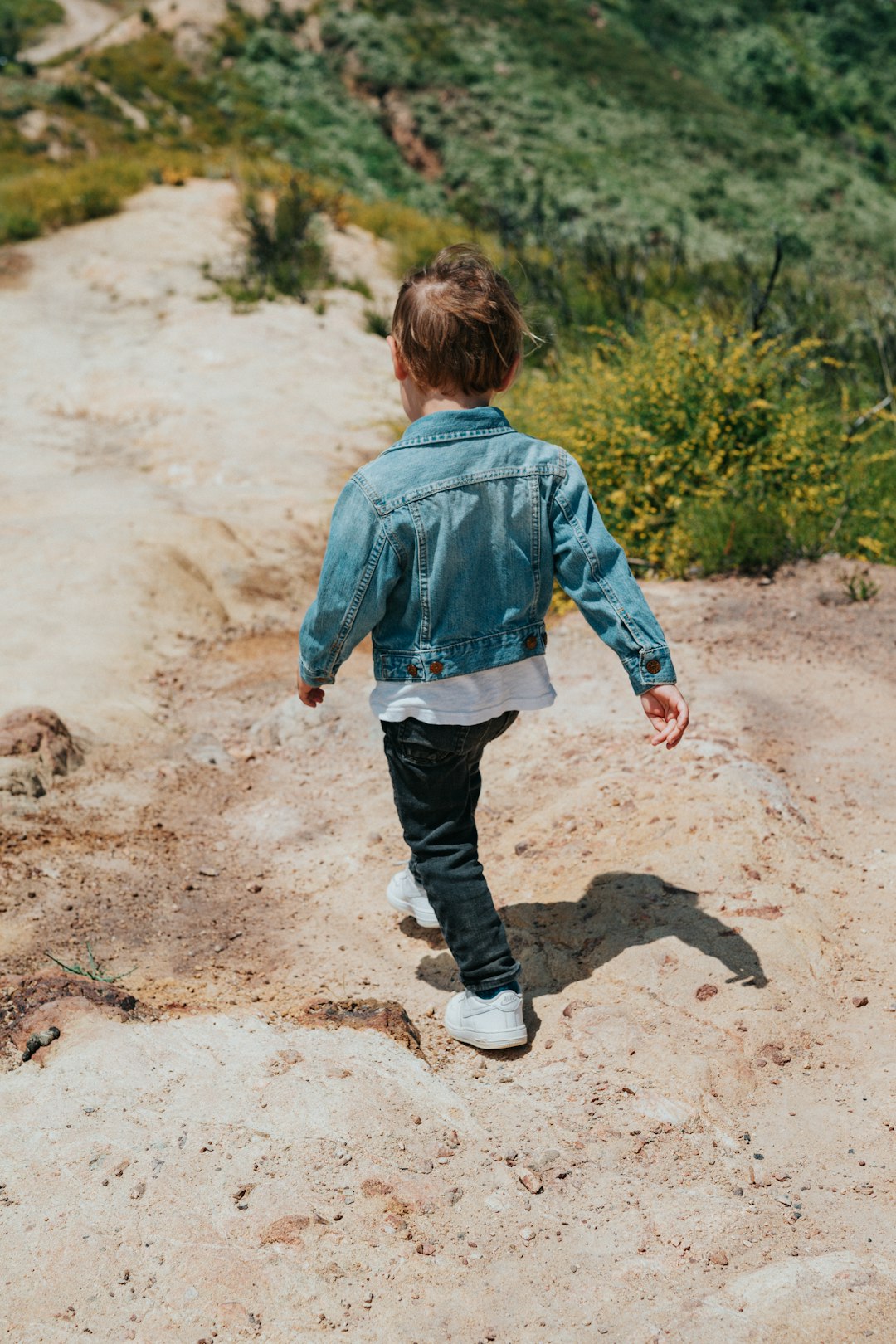 boy in green hoodie and blue denim jeans walking on brown dirt road during daytime