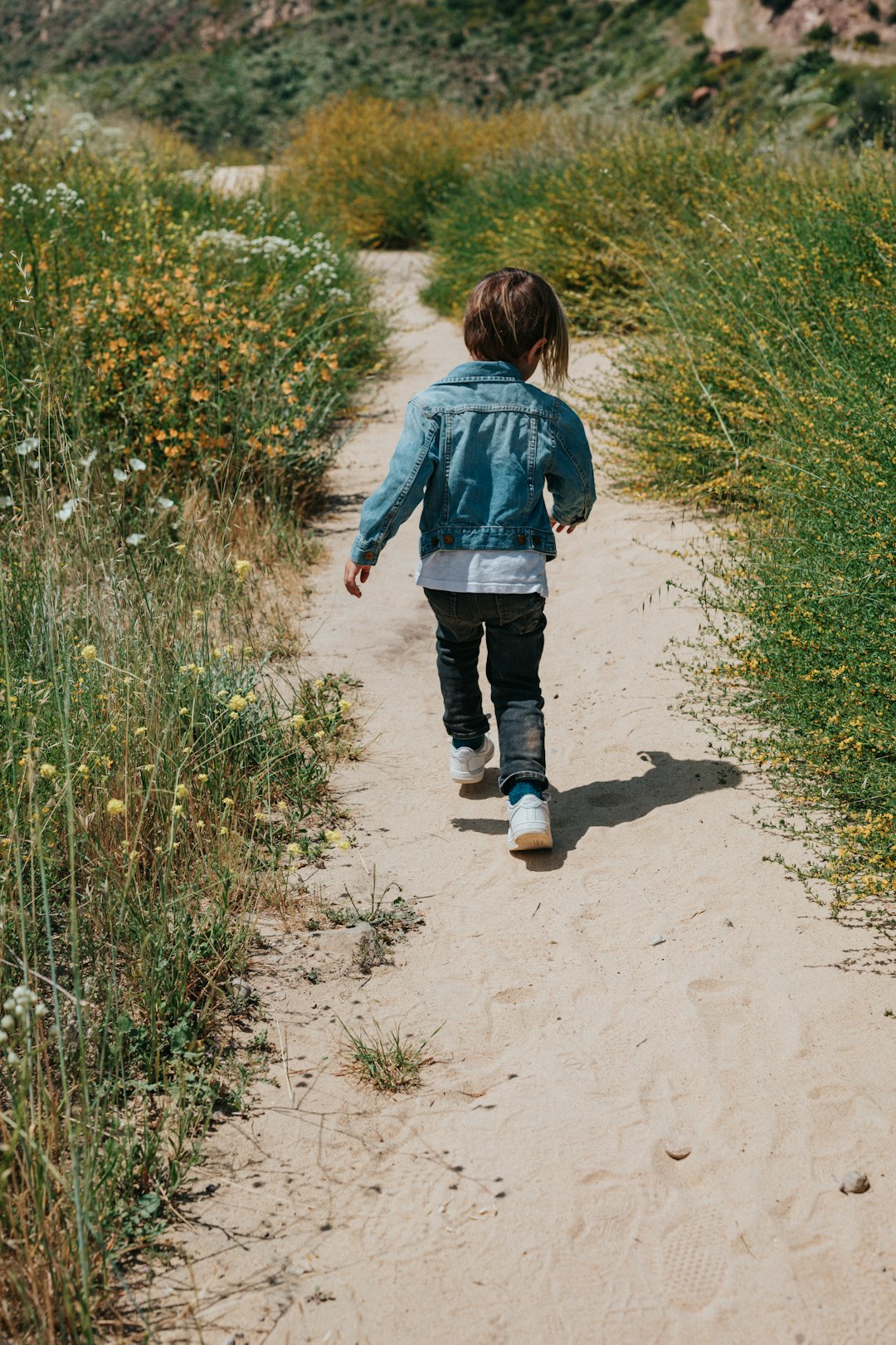 girl in blue jacket walking on dirt road during daytime