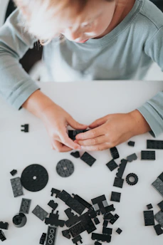 A focused child building a simple robot model on a wooden table filled with educational tools.