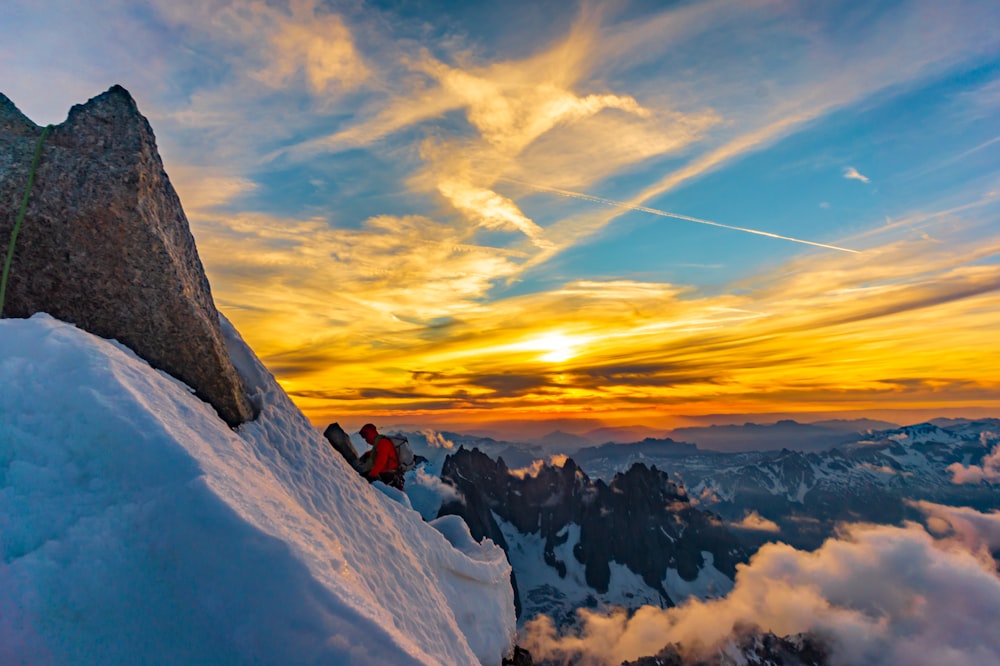 person in red jacket sitting on snow covered mountain during daytime