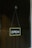 A simple open sign is hanging from a glass door with a suction cup. The sign has a black background with white text, bordered by a light color. The background consists of a dimly lit wooden wall panel.