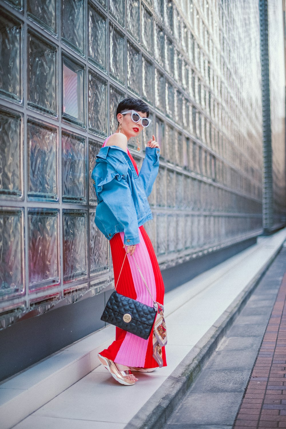 woman in blue jacket and red skirt standing beside train station during daytime