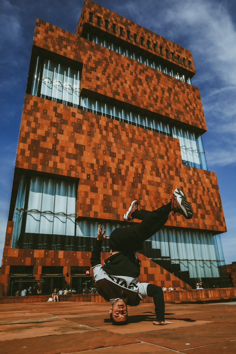 Hombre con chaqueta negra y pantalones negros saltando sobre un edificio de ladrillo marrón durante el día