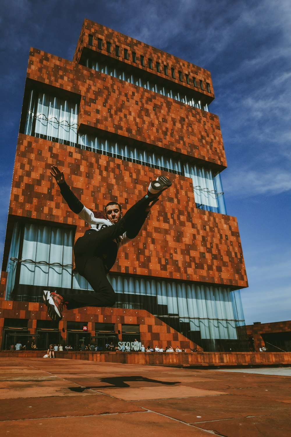 man in black jacket and black pants jumping on brown building during daytime