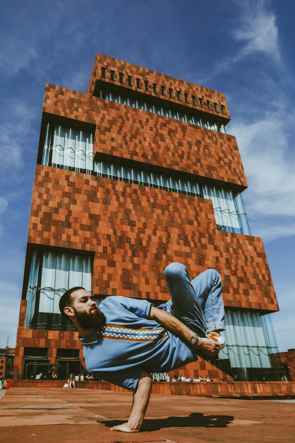 Hombre con camiseta negra y jeans de mezclilla azul parado cerca de un edificio de ladrillo marrón durante el día