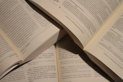 Several open books with visible text in a well-lit setting, showing pages filled with printed paragraphs. The books are arranged in a slightly overlapping manner.