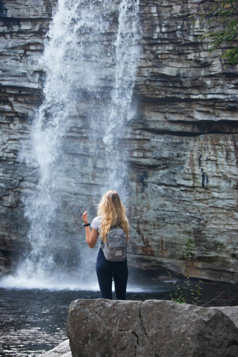 donna in camicia nera a maniche lunghe e leggings neri in piedi vicino alle cascate durante il giorno