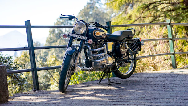 A classic vintage motorcycle parked on a sunlit coastal road in Mallorca, with rolling hills in the background.