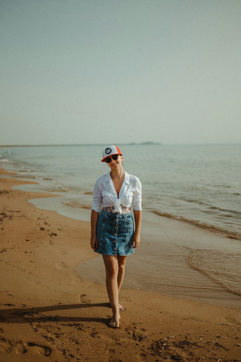 白いシャツとブルーデニムのショートパンツを着た女性が昼間のビーチに立っている