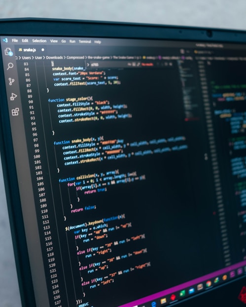 A computer monitor displays a code editor window with JavaScript code. The code appears to be part of a game script, featuring functions related to drawing on a canvas, collision detection, and handling keyboard events. The screen layout indicates the use of Visual Studio Code as the text editor.