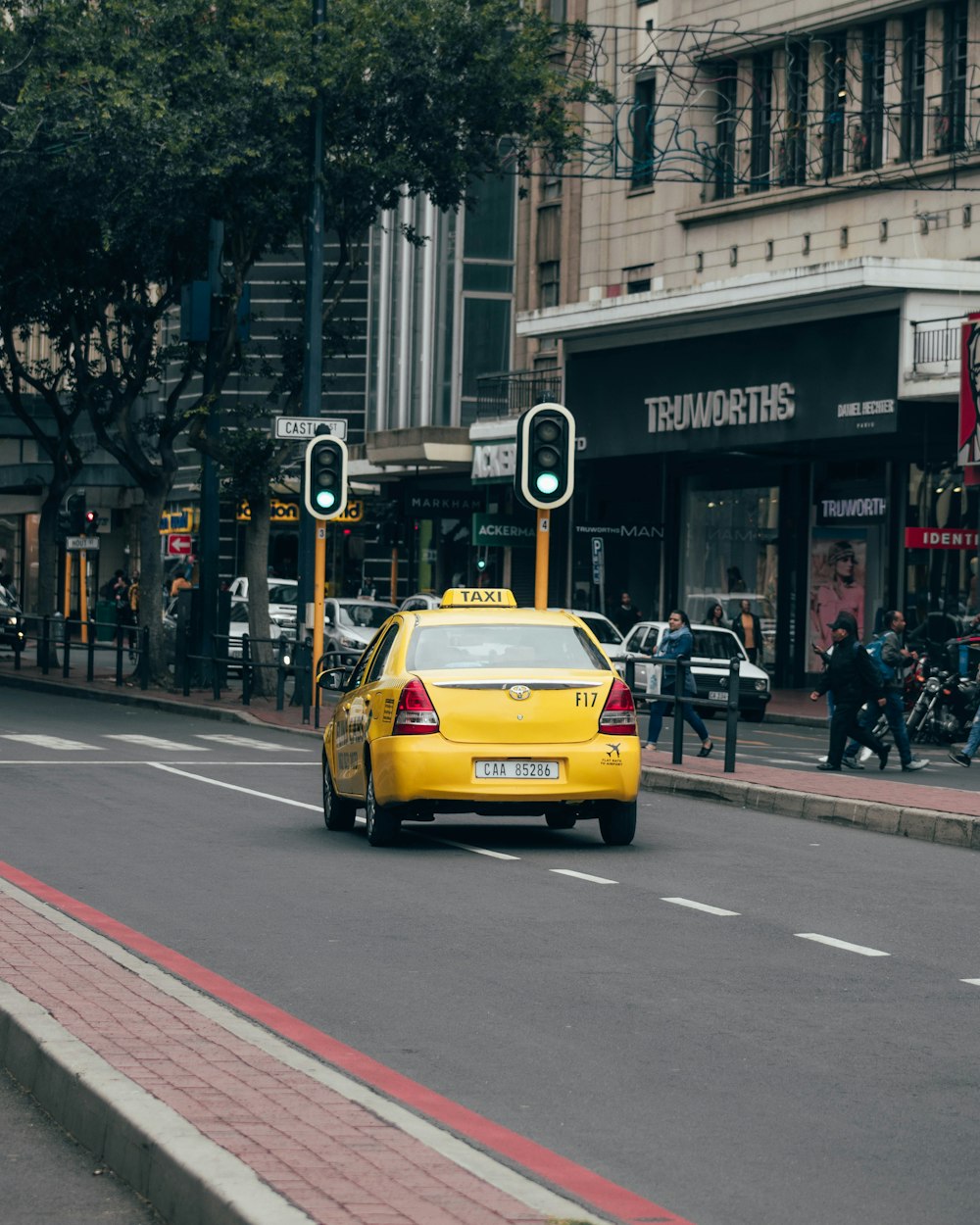 yellow taxi cab on road near people walking on sidewalk during daytime