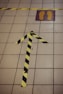 A tiled floor featuring a black and yellow striped tape arrow pointing forward. Adjacent to the arrow is a square marked with footprints inside a yellow and purple rectangle. Another piece of black and yellow tape runs horizontally across the tiles.