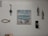 A wall decorated with various nautical-themed items, including a painting of boats on the sea, two hanging fish sculptures, a decorative fishing hook, and a piece of rope shaped like a fish. There is also a small shelf holding a candle.
