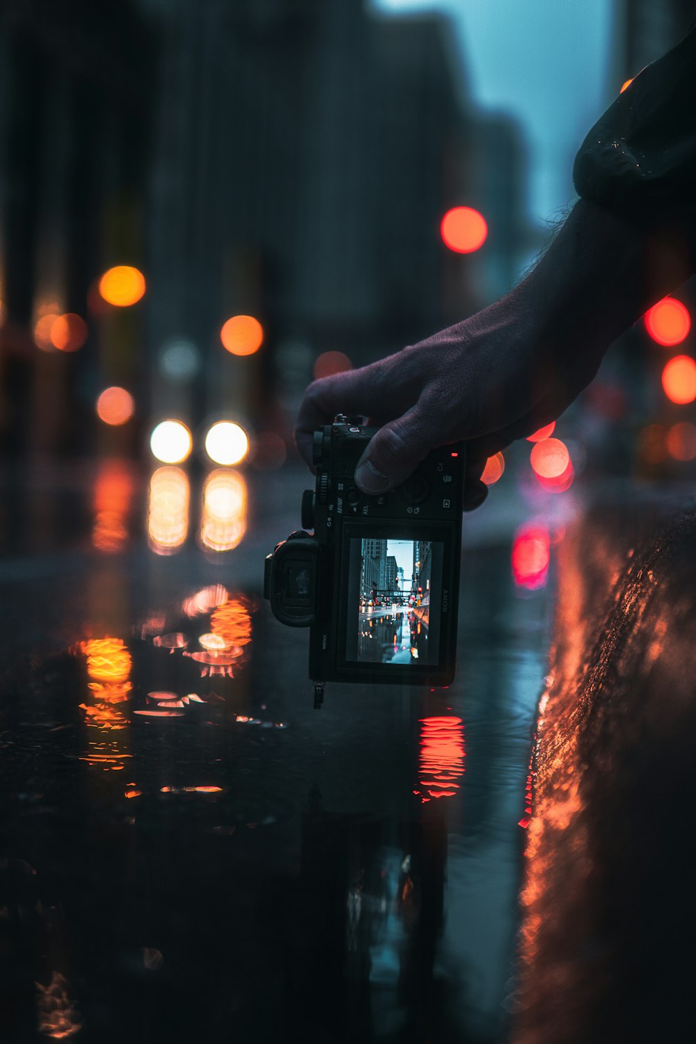 黒いデジタル一眼レフカメラを持っている人が、夜間に街の明かりの写真を撮る