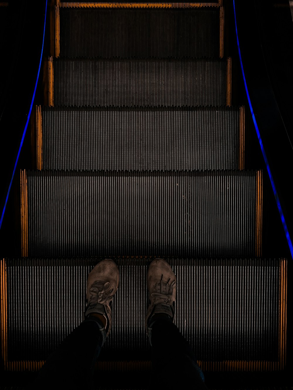 person in gray pants and gray shoes standing on black stairs
