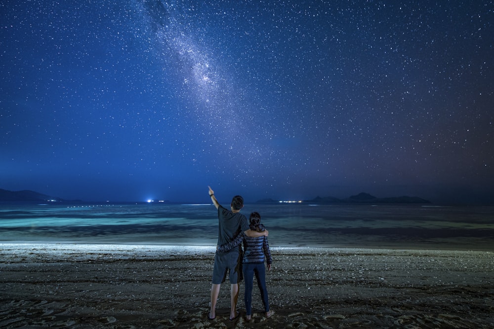 man in black jacket standing on beach shore during night time