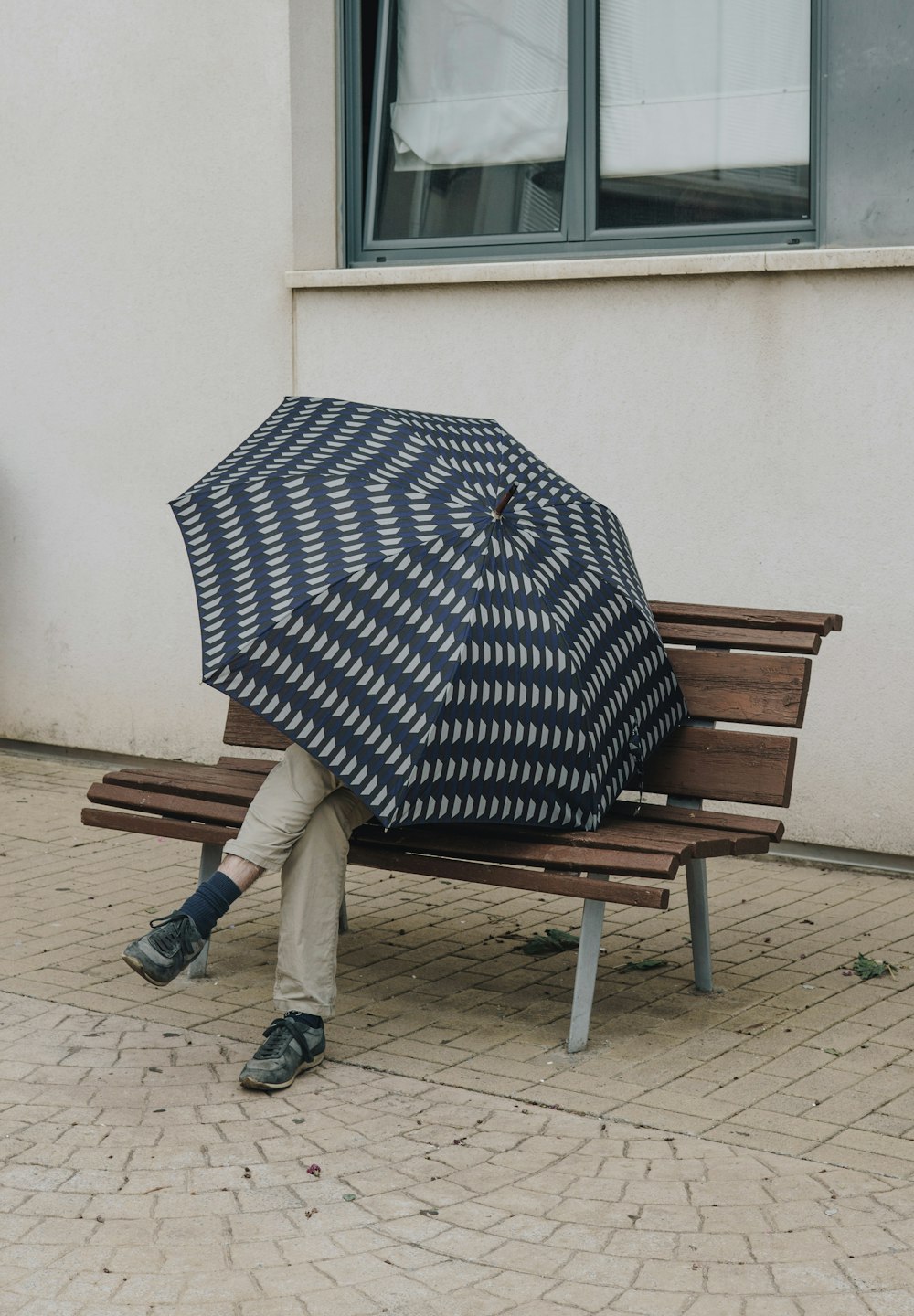 갈색 나무 벤치에 앉아 흑백 물방울 무늬 우산을 쓴 사람