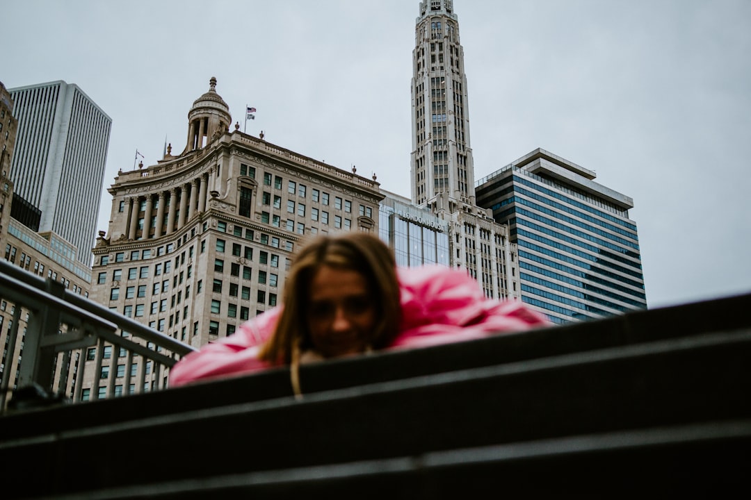 woman in pink hoodie standing near brown concrete building during daytime