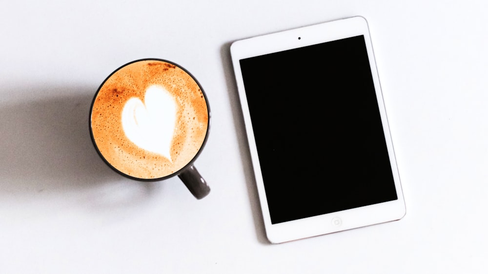 white ipad beside black ceramic mug with brown liquid