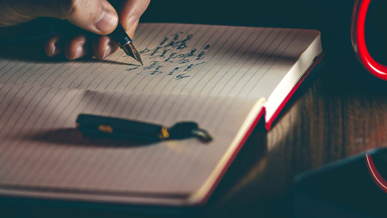 A close-up of hands writing with a fountain pen on textured paper, sunlight casting warm shadows.