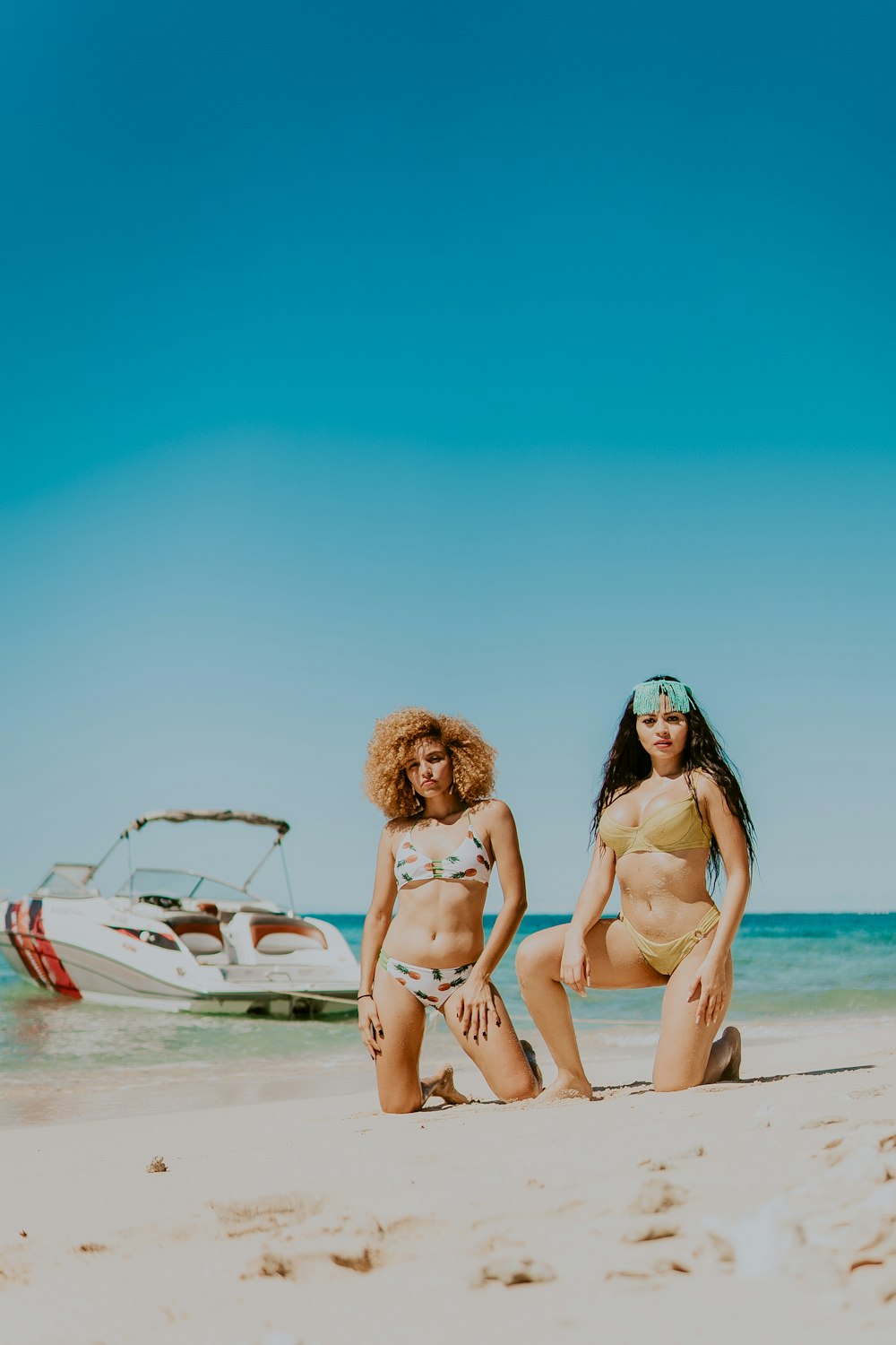 2 mulheres de biquíni sentadas na praia durante o dia