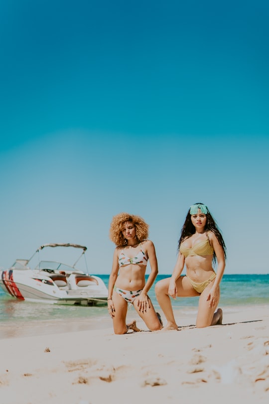 2 women in bikini sitting on beach during daytime in Cayos Cochinos Honduras