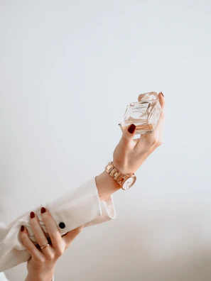 A sophisticated woman applying perfume in a modern, minimalistic room with golden accents.