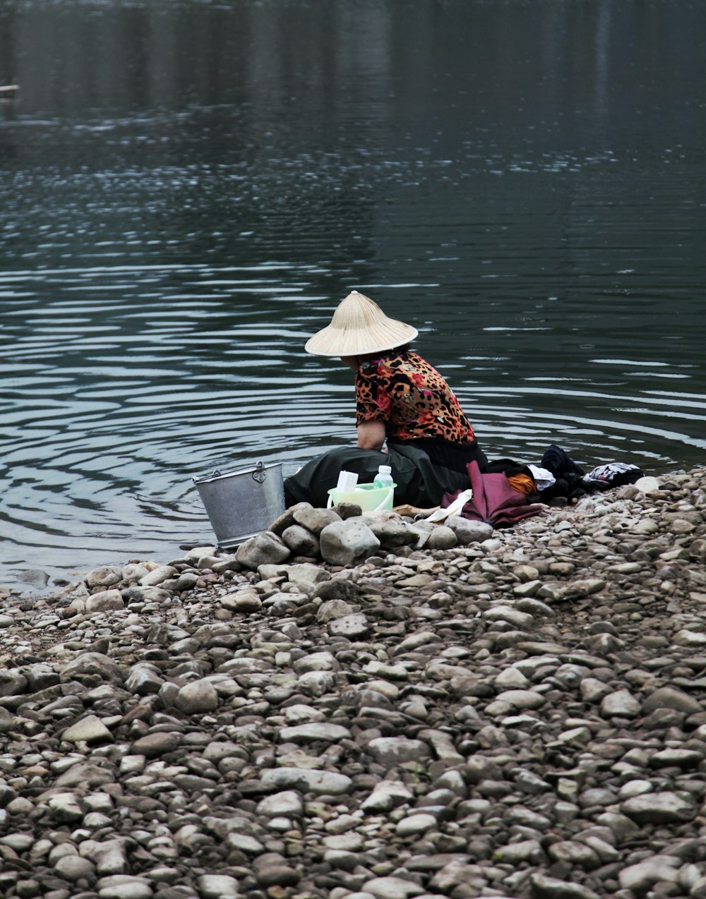 woman in brown sun hat sitting on rocky shore during daytime