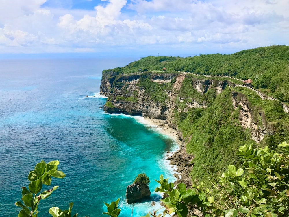 Montaña verde y marrón junto al mar azul bajo el cielo azul durante el día