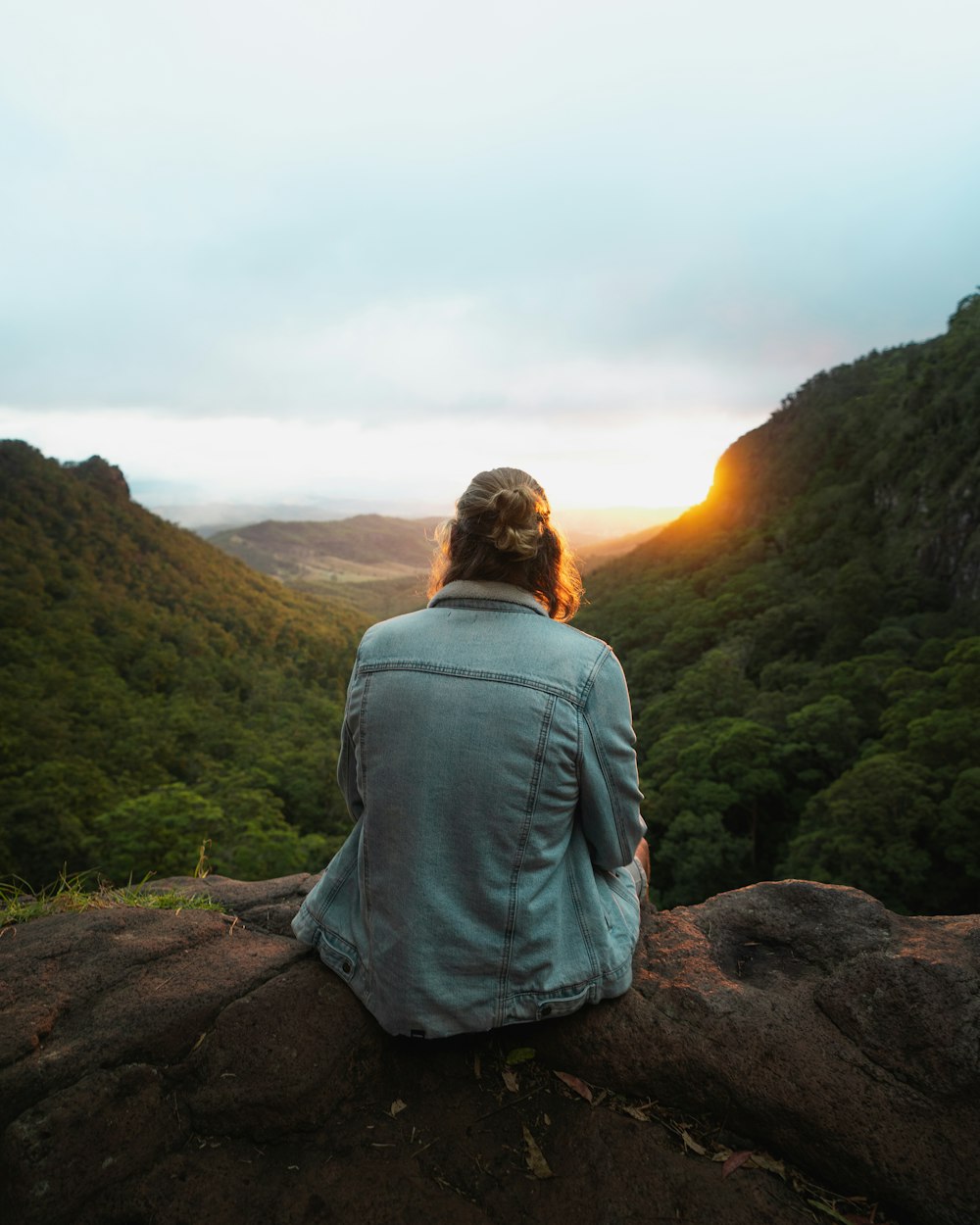 woman in gray jacket sitting on brown rock during daytime