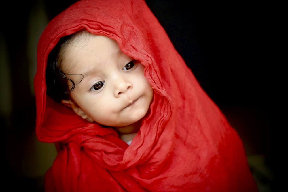 baby in red hoodie lying on red textile