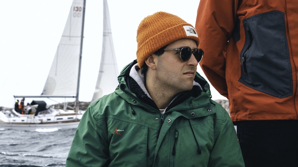 man in green zip up jacket wearing orange knit cap and black sunglasses