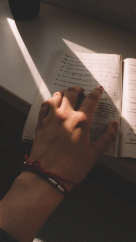 A hand adorned with Luna Gems bracelets resting gently on an open book beside a cup of tea.