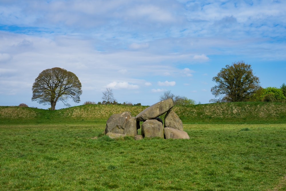 gray rock formation on green grass field under blue and white sunny cloudy sky during daytime