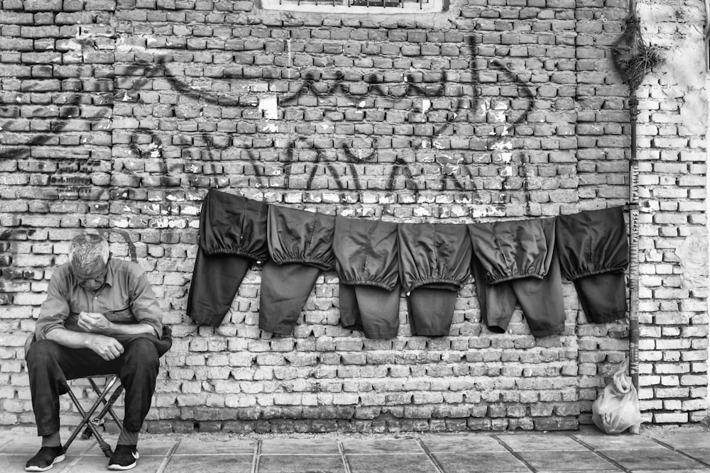 grayscale photo of man in black jacket and pants walking on brick wall